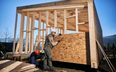 Budowa domów szkieletowych pod klucz. Cennik budowy zależy od projektu. Dwóch budowlańców montuje płyty OSB na drewnianej konstrukcji.