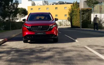 Czerwona Mazda CX-5 jedzie ulicą. W tle budynki i drzewa.