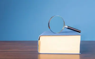 Lente d'ingrandimento su un libro blu, per capire il hic et nunc significato.