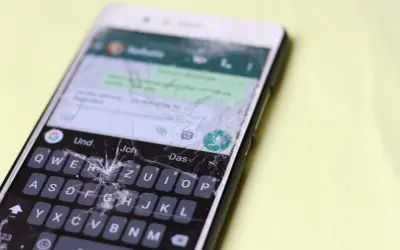Pęknięty ekran telefonu wymaga pilnej wymiany. Widać klawiaturę i fragmenty rozmowy.