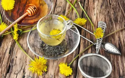 Aromatyczny napar z mlecza w szklanej filiżance, obok miodu i świeżych kwiatów.