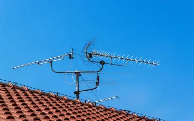 Na dachu domu, pod błękitnym niebem, zamontowana jest wieloelementowa antena TV.