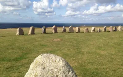 Rząd kamieni Ales Stenar na trawiastym polu, z morzem i chmurami w tle.