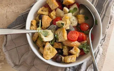 Herzhafter Brotsalat mit Roggenbrot, Kirschtomaten, Oliven und Artischockenherzen, garniert mit frischen Kräutern.
