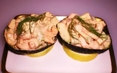 Zwei Avocadohälften gefüllt mit einem cremigen Krabbencocktail mit Avocado und Dill garniert, serviert auf Zitronenscheiben.