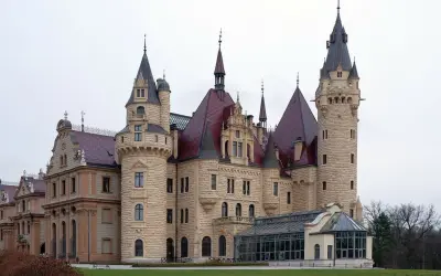 Imponujące pałace w Polsce, z wieżami i czerwonymi dachami, otoczone zielenią.