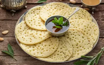 Une assiette de crêpes mille trous dorées, garnie d'une coupelle de miel et de menthe fraîche. Parfait pour un petit-déjeuner gourmand.
