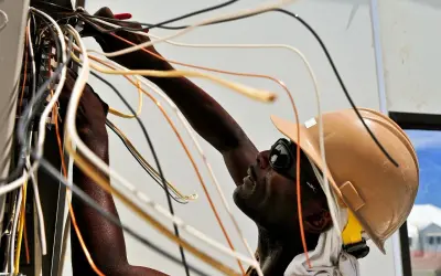 Elektryk w kasku i okularach pracuje przy instalacji elektrycznej, łącząc przewody. To dobry przykład, jak zostać elektrykiem.