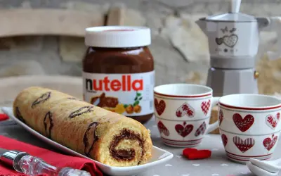 Rotolo alla Nutella pronto per essere gustato, con una moka e due tazze a tema cuore.