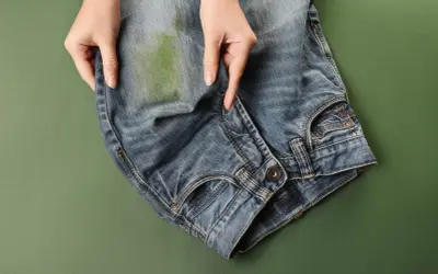 Mani che indicano una macchia verde su jeans, per mostrare come togliere macchie di jeans su ecopelle.