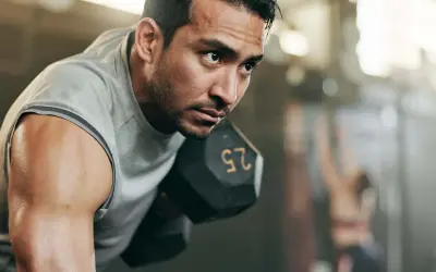 Fokusierter Mann hebt Hantel. Sein Schweiß glänzt. Ein Teil eines 2er Split Trainingsplans.
