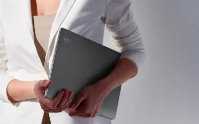 Kobieta w białej marynarce trzyma laptopa Lenovo Yoga. Czas na aktualizację systemu, by praca była płynna.