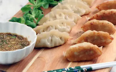 En rad gyllene, stekta dumplings och ångade dumplings serveras med en dippsås och grönsaker. Ett perfekt dumplings recept för en god måltid.
