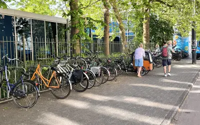 Viele Fahrräder stehen am Straßenrand, ein Mann mit Kind auf dem Arm und eine Frau mit Lastenrad gehen vorbei. Eine echte Stadt der kurzen Wege.