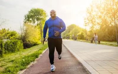 Glücklicher Mann beim Laufen im Park. Sein Training laufen im Sonnenschein macht ihn fit und gesund.
