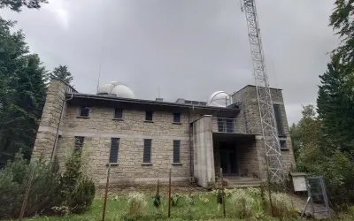 Obserwatorium na Lubomirze, kamienny budynek z kopułami teleskopów i wieżą telekomunikacyjną, otoczony zielenią.
