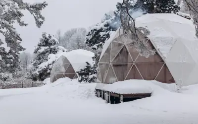 Śnieżne krajobrazy i przytulne domki do wynajęcia na weekend. Dym unosi się z komina jednego z igloo, zapraszając do środka.