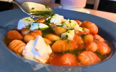 Pyszne makaron gnocchi z pomidorami, mozzarellą i zielonym sosem. Łyżka z sosem czeka na dodanie.