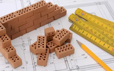 Miniaturowa budowa na planie architektonicznym: cegły, miarka i ołówek. To jakby planistyczna zabawa w budowanie.