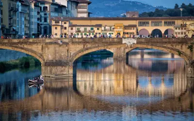 Le Ponte Vecchio à Florence, avec ses maisons colorées et ses reflets sur l'Arno. Une barque navigue paisiblement sous le pont.