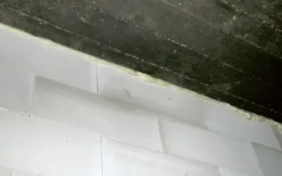 Piana montażowa, która jest rodzajem **elastomery**, uszczelnia połączenie między betonową belką a białymi bloczkami.