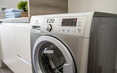 Pralka Electrolux z wyświetlonym błędem E20. Na blacie obok stoją złożone ręczniki i roślina.