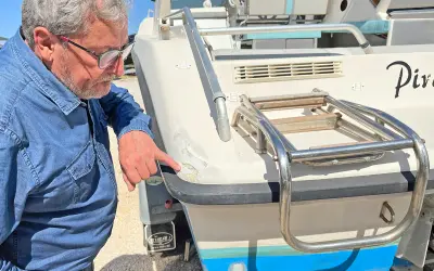 Un homme examine les dégâts sur le gelcoat d'un bateau. C'est quoi le gelcoat ? C'est la couche protectrice extérieure.