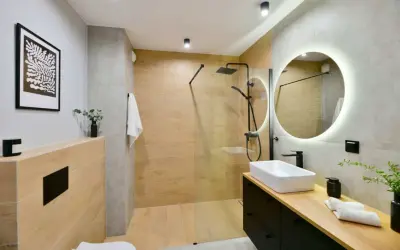 Baño moderno con ducha de suelo continuo, lavabo sobre encimera y espejo circular iluminado.