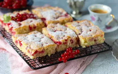 Saftiger Johannisbeer Kuchen, mit Puderzucker bestäubt, auf einem Gitterrost, daneben eine Tasse Kaffee und frische Johannisbeeren.