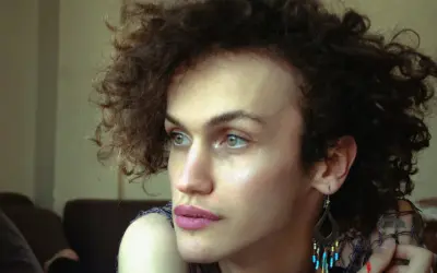 Portret osoby z kręconymi włosami, która zastanawia się nad przyczynami dysforii płciowej.