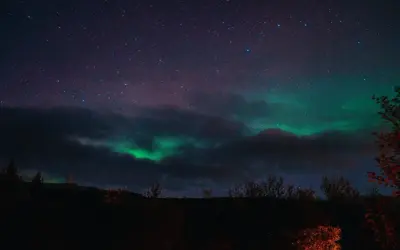 Zielona zorza polarna tańczy na nocnym niebie nad Islandią, wśród gwiazd i ciemnych chmur.