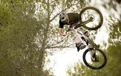 Tomas Lemoine fliegt mit seinem Mountainbike durch die Luft, umgeben von Bäumen.