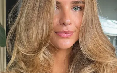 Piękna kobieta z falowanymi włosami w odcieniu maślany blond. Jej oczy są zielone, a usta delikatnie umalowane.
