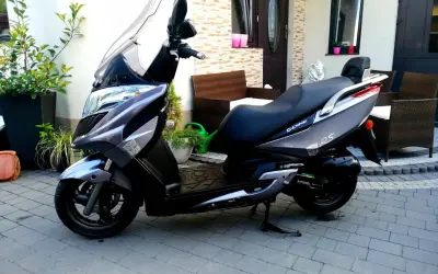 Elegancki skuter Kymco Dink 50 w kolorze grafitowym stoi na podjeździe, gotowy do jazdy.