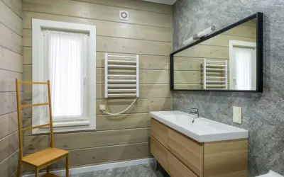 Salle de bain moderne avec murs en bois clair et pierre grise. Un meuble vasque en bois, un miroir, un radiateur et une échelle en bambou pour habiller un mur.