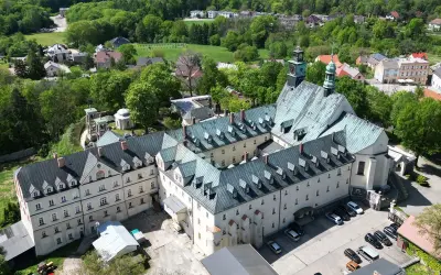 Widok z lotu ptaka na klasztor na Górze Świętej Anny. Rozległy kompleks budynków z zielonymi dachami otoczony bujną zielenią.