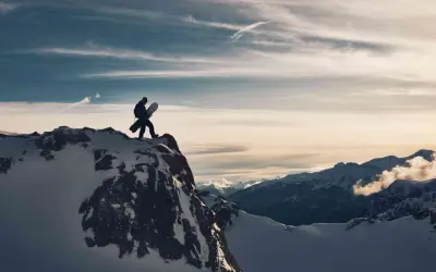 Sylwester w Alpach: snowboardzista na szczycie góry, gotowy na zjazd. W tle majestatyczne, ośnieżone szczyty i dramatyczne chmury.