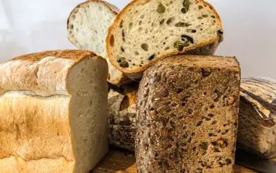 Różne rodzaje chleba, w tym bochenek z oliwkami i chleb żytni z ziarnami.
