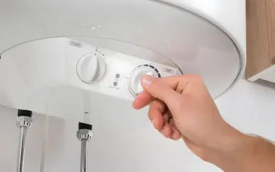 Mano ajustando el termostato de un termo eléctrico. Averigua cuanto dura un termo eléctrico y optimiza su uso.