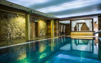 Basen w hotelu Aubrecht Country Spa Resort Koprzywnica. Woda w basenie ma piękny, turkusowy kolor, a ściany zdobi kamień i drewno.