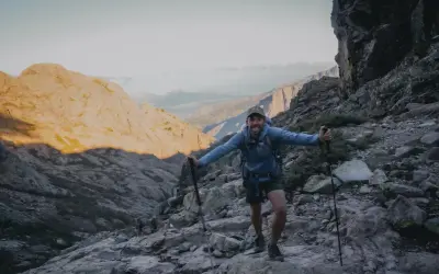 Un randonneur souriant sur un sentier rocheux, bâtons en main. Il semble se demander quel est le gr le plus difficile.