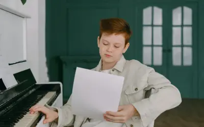 Chłopiec z rudymi włosami ćwiczy grę na pianinie, studiując nuty. Może właśnie poznaje nazwy oktaw, przygotowując się do występu.