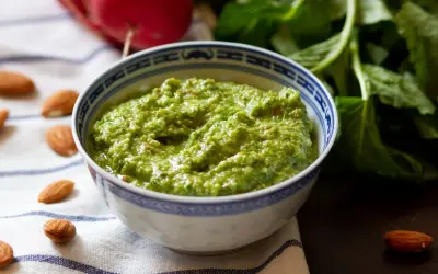 Pesto z liści rzodkiewki, z migdałami i świeżymi ziołami, w miseczce z niebieskim wzorem.