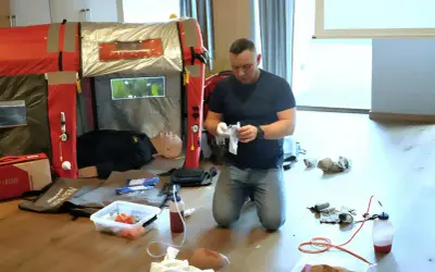 Ćwiczenia praktyczne podczas kpp kurs. Instruktor przygotowuje sprzęt medyczny obok manekina.
