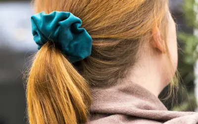 En hästsvans med en turkos scrunchie i sammet. Håret är kopparfärgat och faller mjukt.