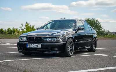 Czarne BMW E39 na parkingu, z widocznym przodem i bokiem samochodu.