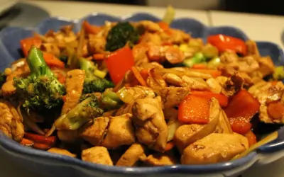 En blå skål fylld med wokad kyckling, broccoli, paprika och morötter. En läcker och färgstark måltid.
