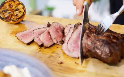 Perfekt grillad ryggbiff skärs upp på en skärbräda. Bredvid ligger en grillad citronhalva.