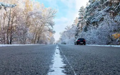 Droga przez zaśnieżony las. Czarny lód na jezdni, drzewa pokryte szronem. Samochód jedzie w stronę widza.