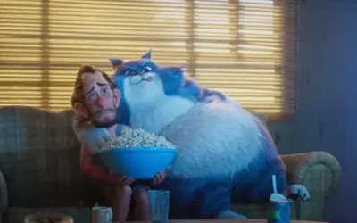 Wielki, niebieski kot przytula zmartwionego mężczyznę, który trzyma miskę popcornu. To scena z filmu "Jak pies z kotem", gdzie relacje między zwierzętami a ludźmi bywają skomplikowane.